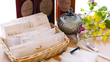 A variety of personal care items including hairbrushes, razors, and a cotton kit, along with body soap and shampoo, arranged on a table with a decorative glass container and flowers.