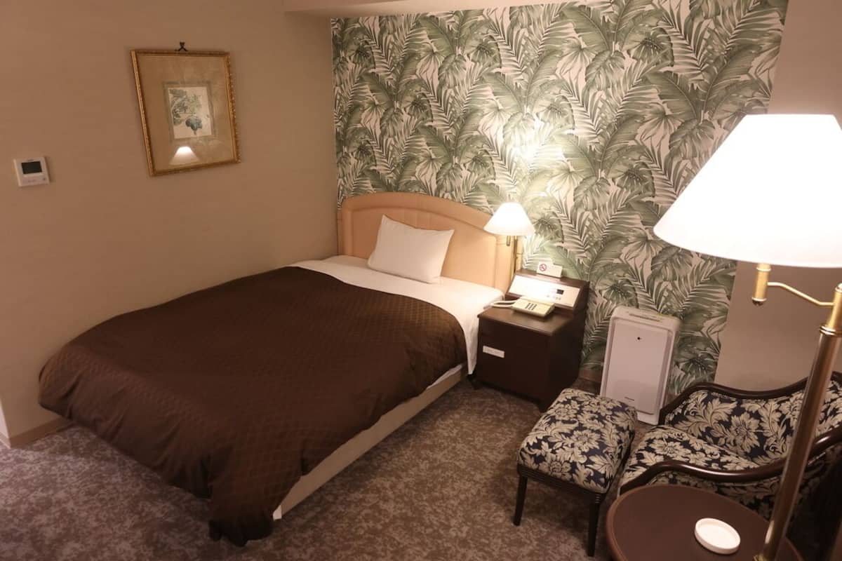 A hotel room with a bed, bedside tables, a lamp, a chair, and a small table.