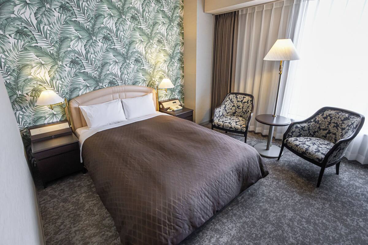 A hotel room with a large bed, two nightstands, a chair, and a lamp.