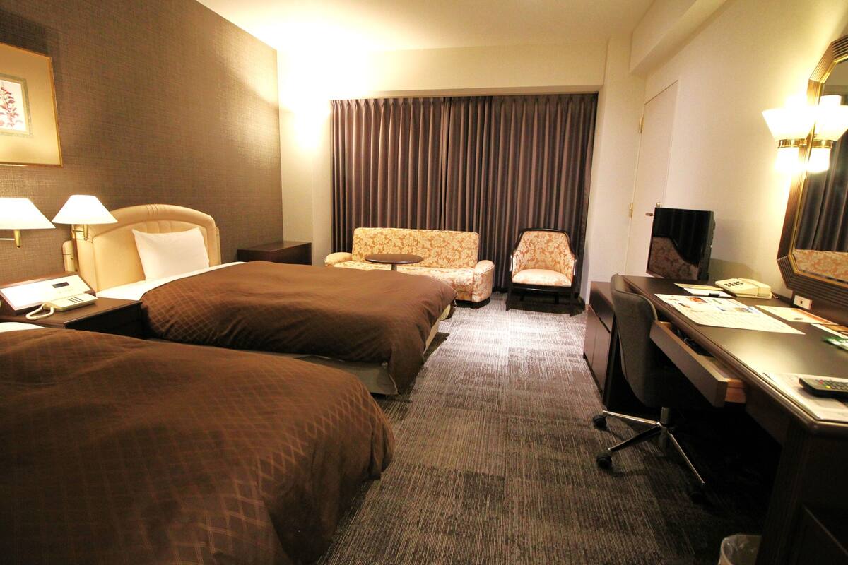 A hotel room with two beds, a desk, a chair, a small table, and a large mirror.