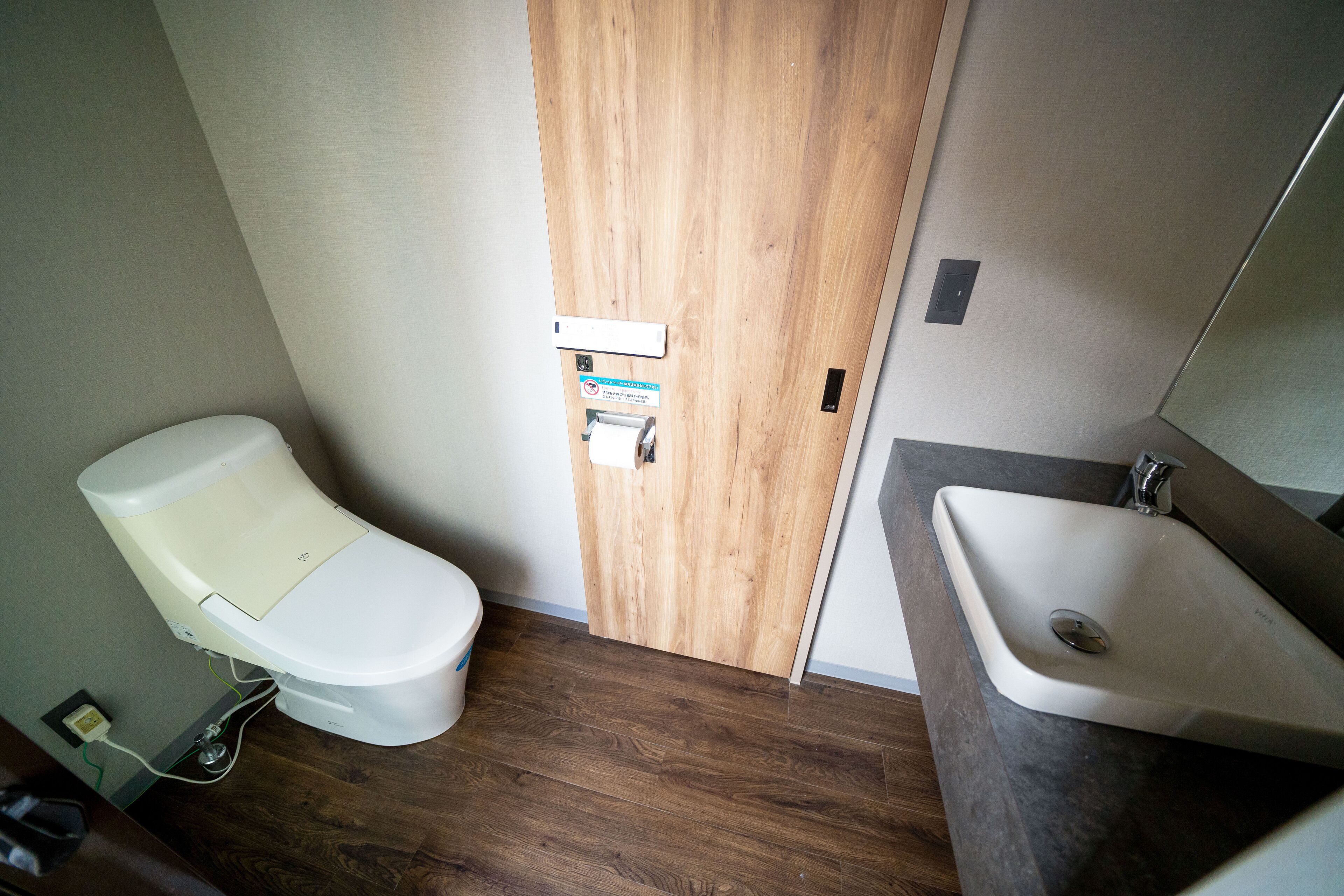 A small bathroom with a toilet, wooden door, and a sink with a mirror.