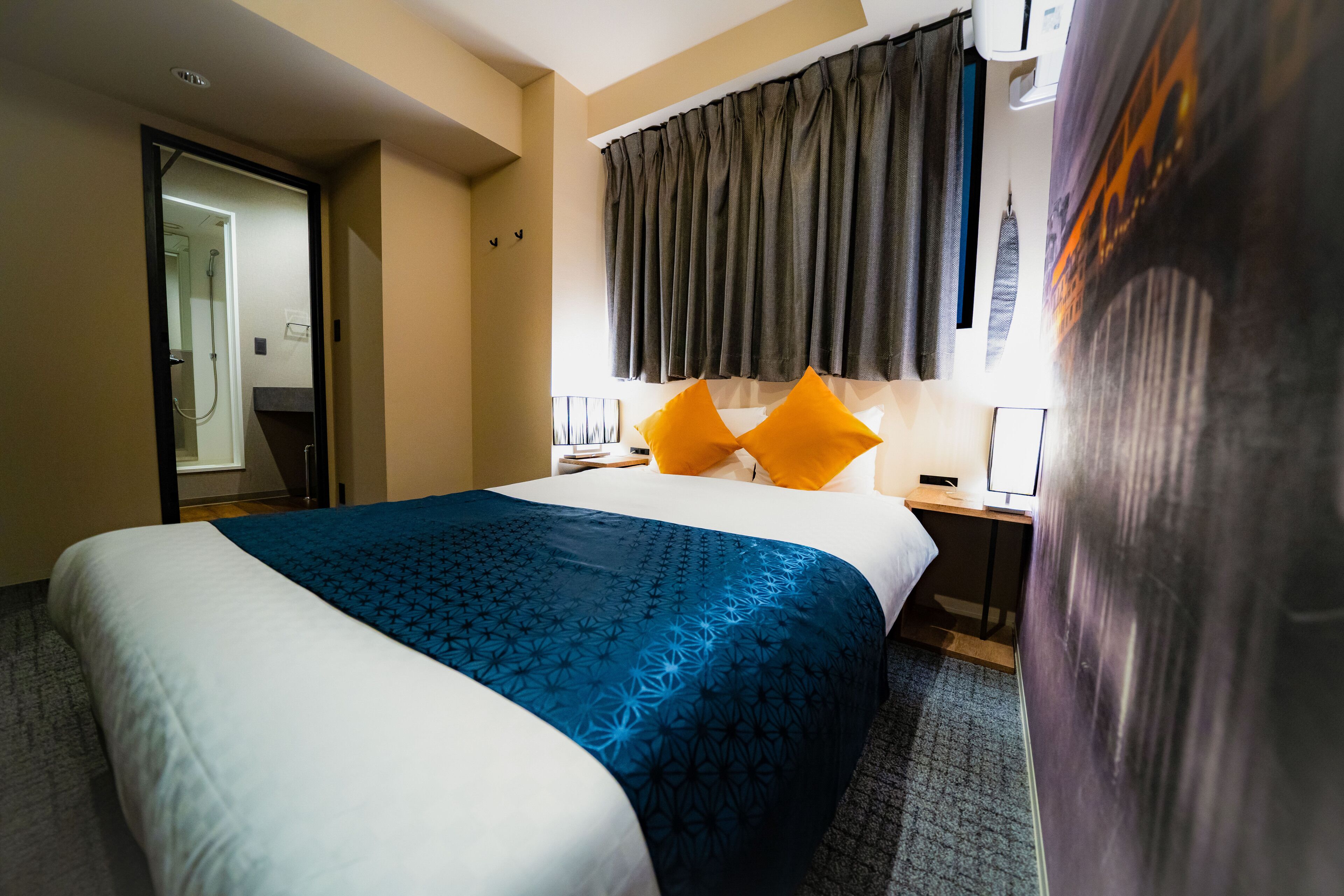 A hotel room with a bed, a nightstand, a desk, and a window with curtains.