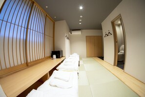 Una habitación con esteras de tatami, un banco de madera y una cama futón con ropa de cama blanca.