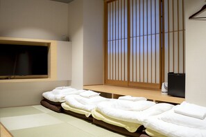 Una habitación tradicional japonesa con suelo de tatami, un divisor corredizo tipo shoji y un televisor fijado a la pared.