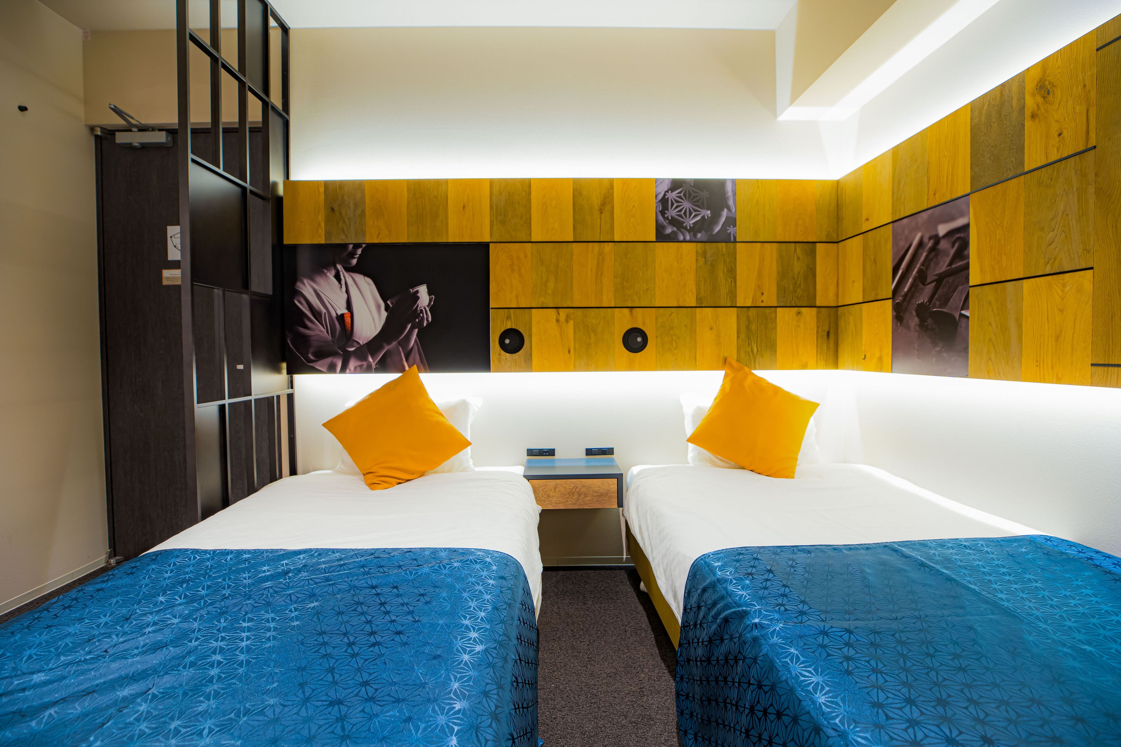 A hotel room with two beds, a wooden accent wall, and a nightstand with a lamp.