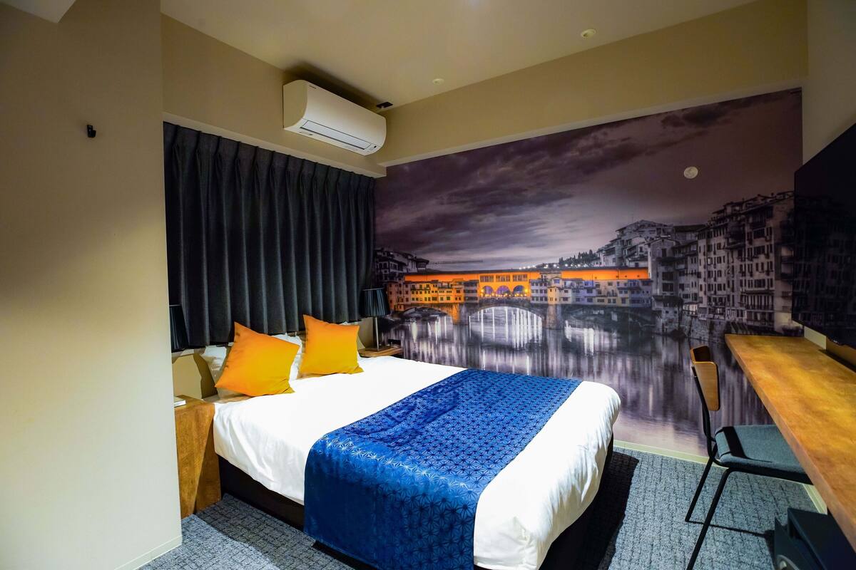 A hotel room with a bed, a desk, and a large cityscape mural on the wall.