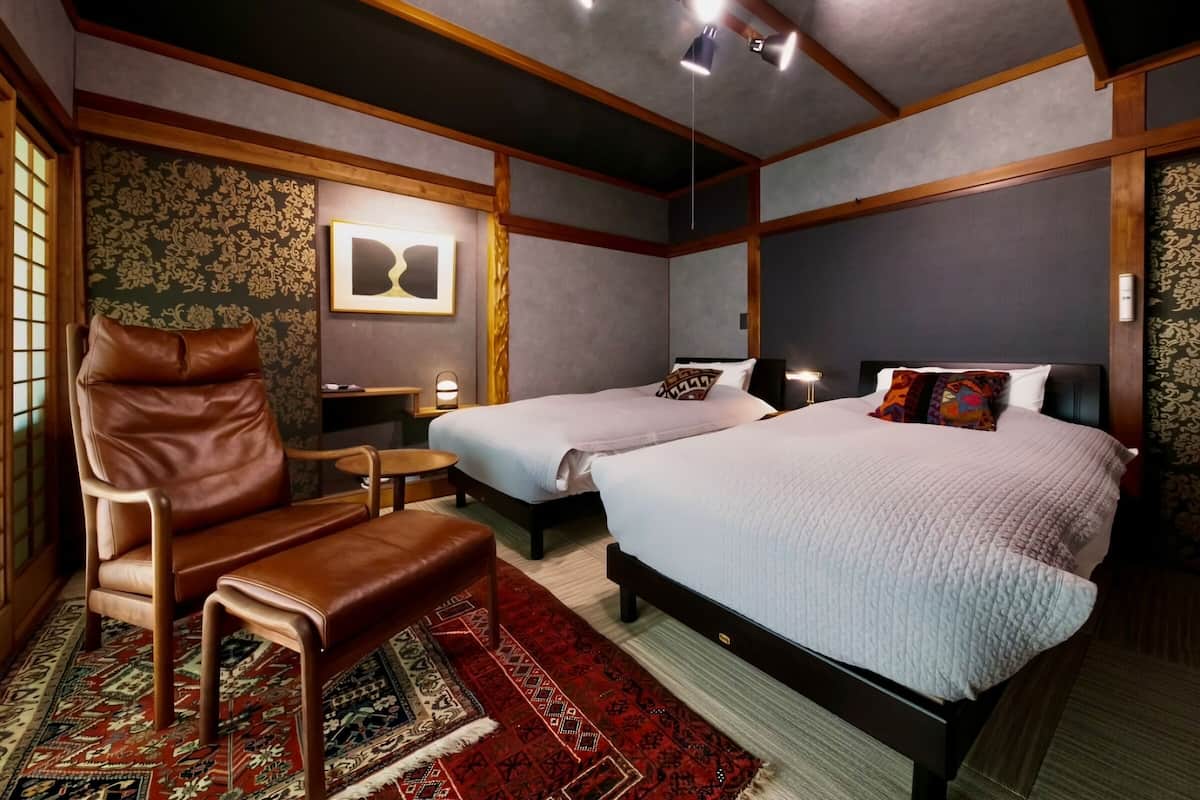 A hotel room with two beds, a leather chair, a small table, and a decorative rug.