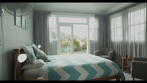 A bedroom with a bed, a chair, a standing fan, and a view of the outdoors. - Top of the Town (Picton)