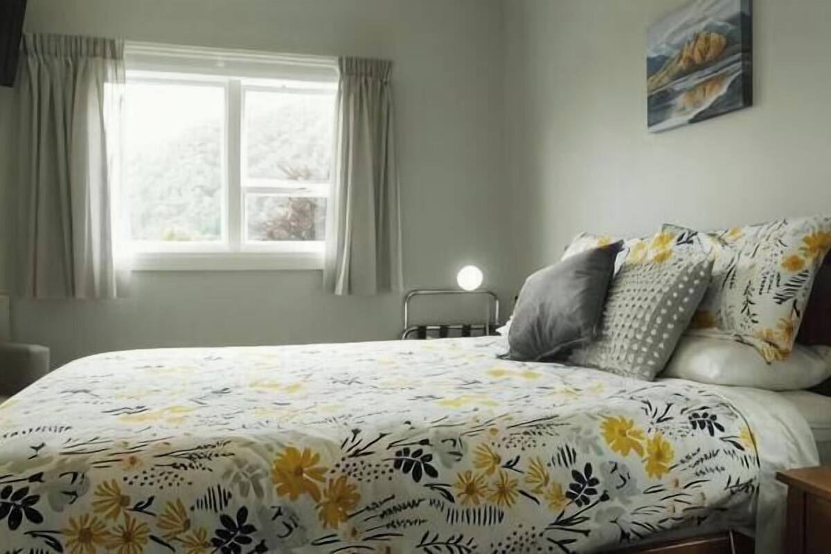 A bedroom with a bed, a window with curtains, a bedside table, and a wall-mounted lamp.