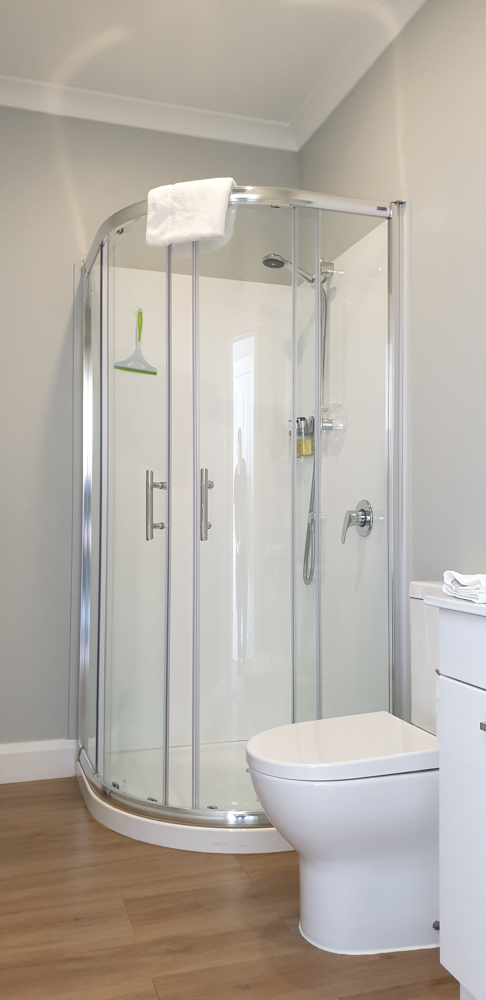 A modern bathroom with a glass-enclosed shower, a white toilet, and a wooden floor.