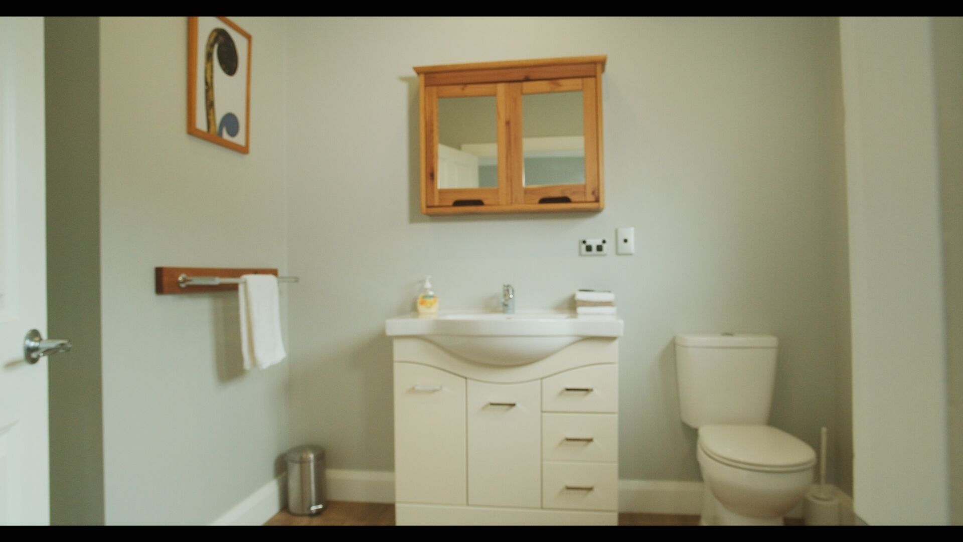 A bathroom with a white sink, wooden cabinet, and a toilet.