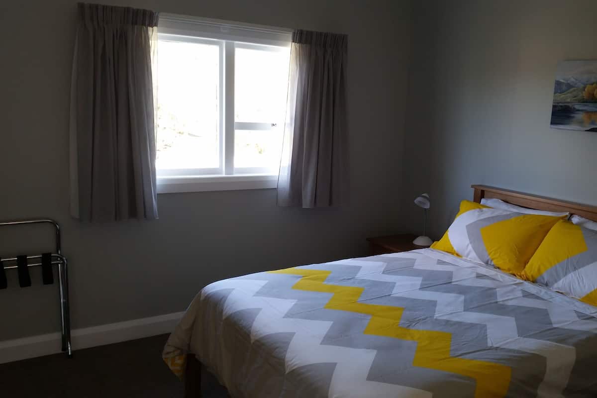 A bedroom with a bed, a window with curtains, a bedside table, and a wall-mounted painting.