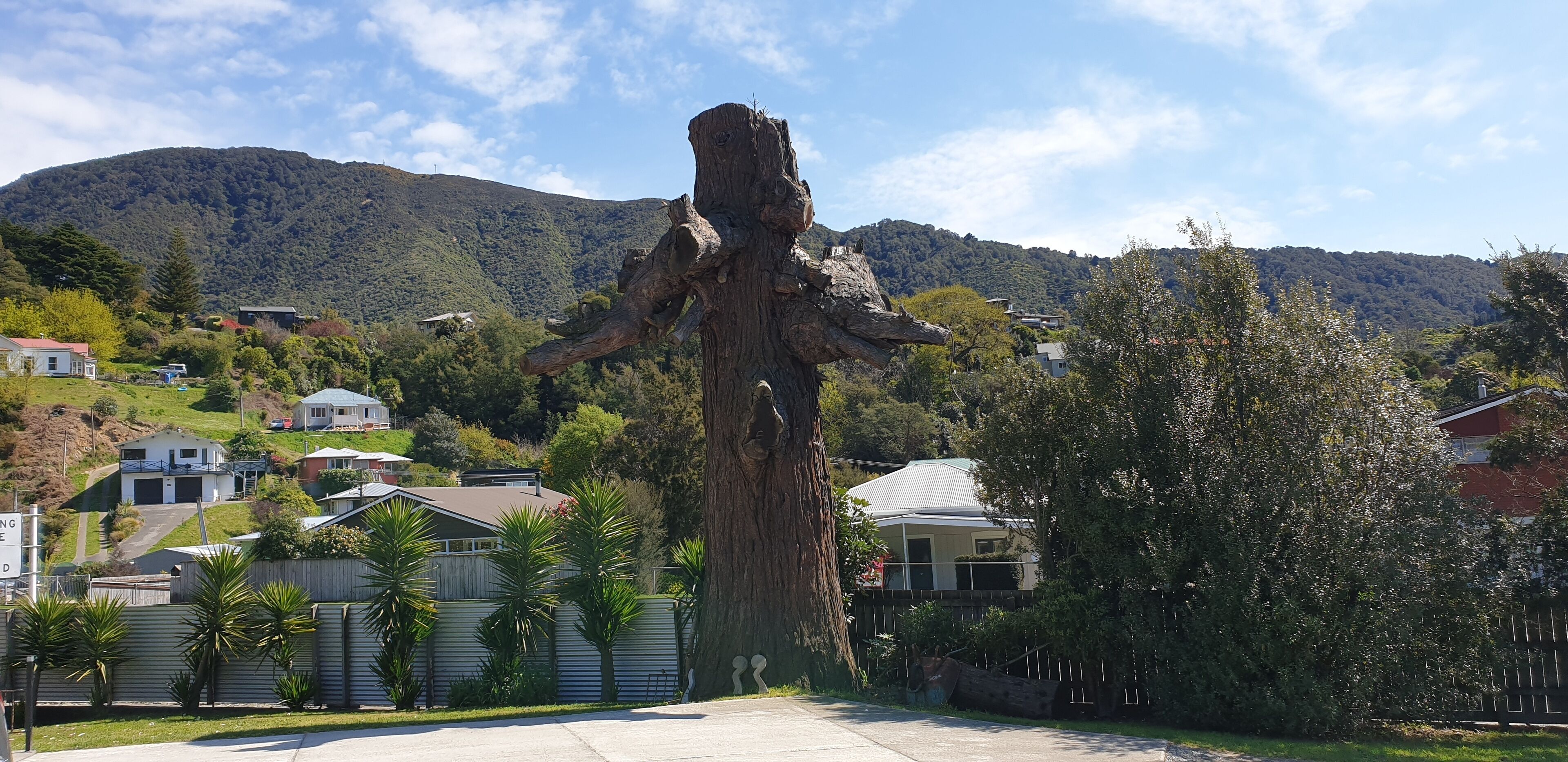A large tree sculpture in a residential area with houses and a mountain in the background.