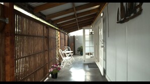 A narrow corridor with a wooden fence on one side and a white door on the other. There is a small table and chairs in the center, and a potted plant with pink flowers at the end of the corridor. - Top of the Town (Picton)