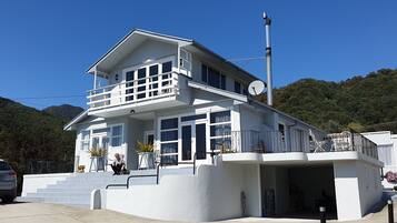 Un edificio bianco a due piani con un balcone, dei gradini che conducono all'ingresso e un'antenna parabolica sul tetto.