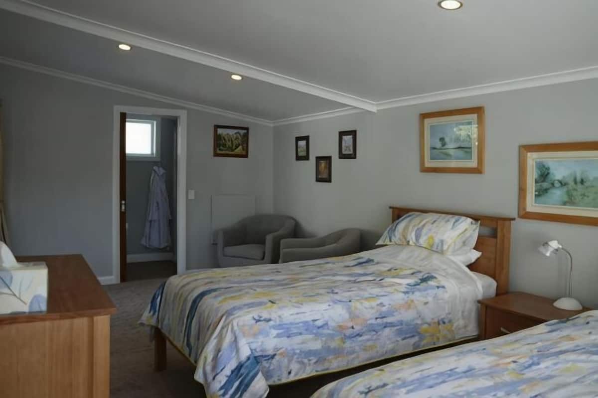A bedroom with two beds, a desk, a chair, and a door leading to another room.
