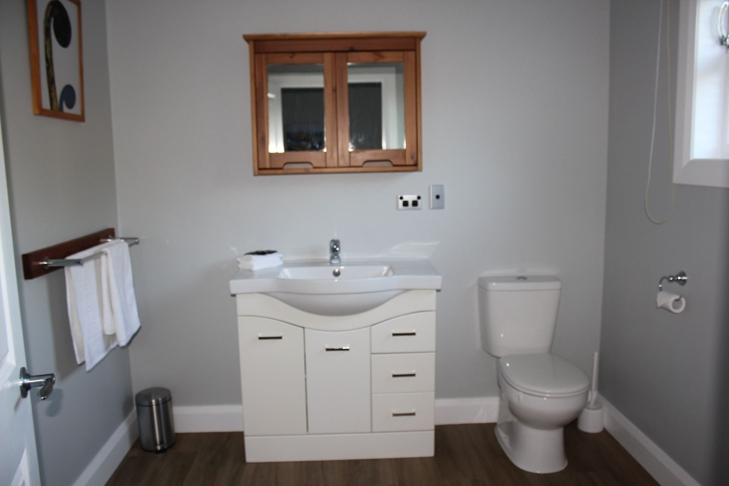 Un baño con lavamanos blanco, un mueble de madera y un inodoro.