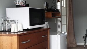 A bedroom with a wooden dresser, a white microwave, a television mounted on the wall, and a bed with a blue and white patterned bedspread. - Top of the Town (Picton)