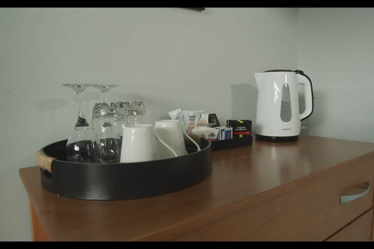 A wooden table with a black tray holding wine glasses, a white mug, and a coffee maker.
