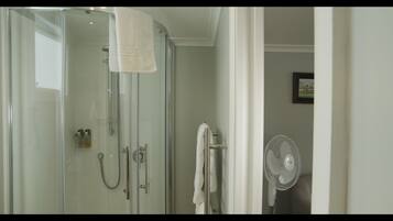 A glass-enclosed shower with a towel hanging on the door, a handheld showerhead, and a wall-mounted fan.