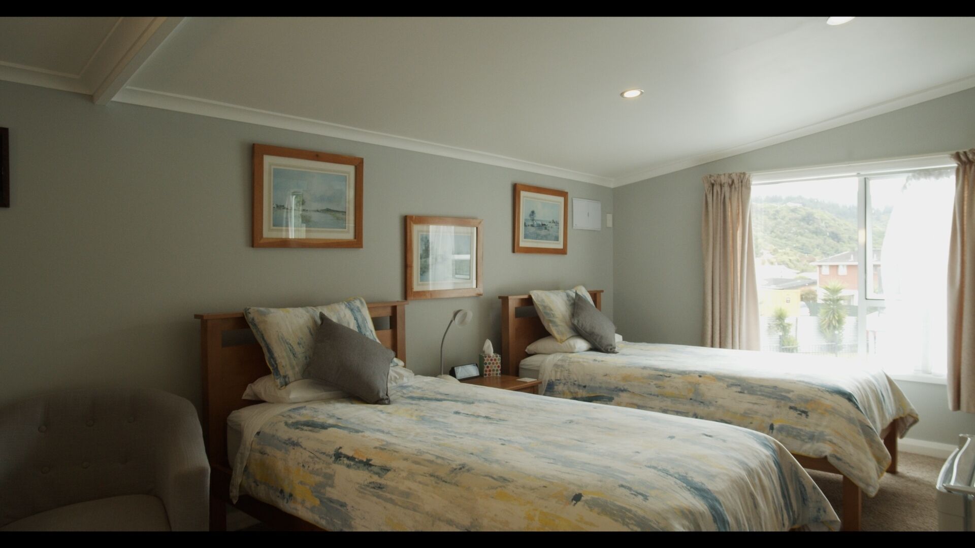 Une chambre d’hôtel avec deux lits, une chaise et une fenêtre donnant sur l’extérieur.