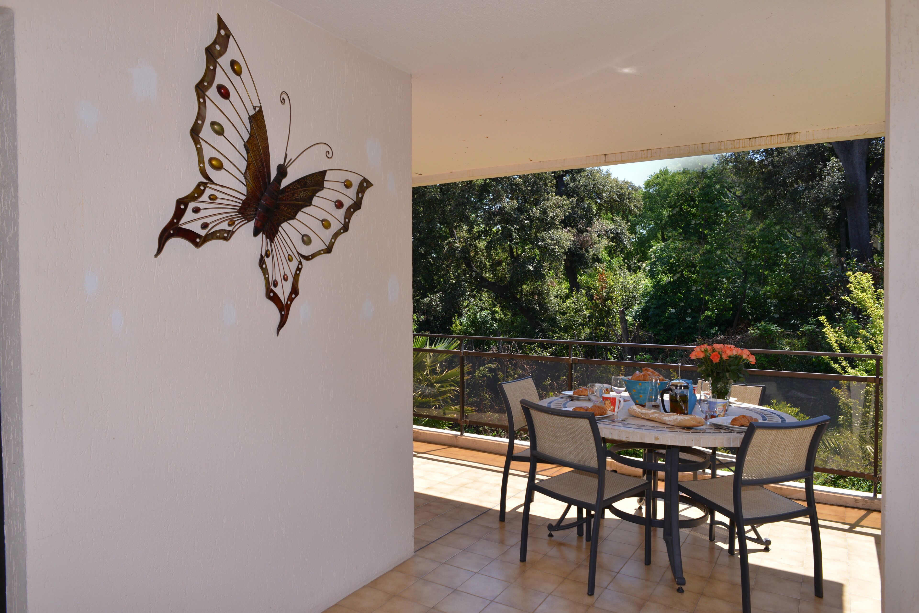 A balcony with a dining table, chairs, and a butterfly wall art.
