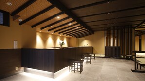 A reception area with a dark reception desk, wooden stools, a potted plant, and a traditional Japanese sliding door. - Onyado Nono Nara Natural Hot Spring (Nara)