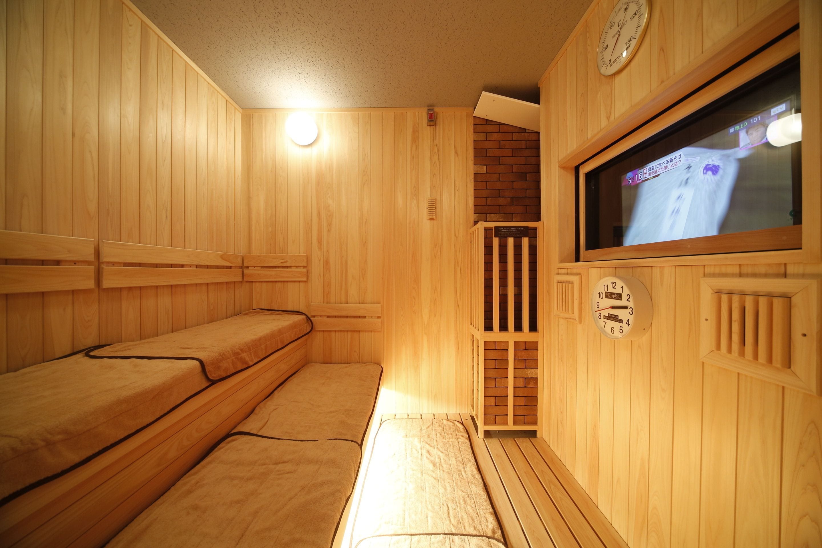 Una sauna de madera con bancos, una pantalla de televisión y un reloj en la pared.