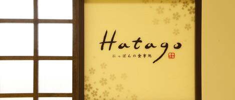 Un cartel enmarcado con el nombre "Hatago" y texto en japonés.