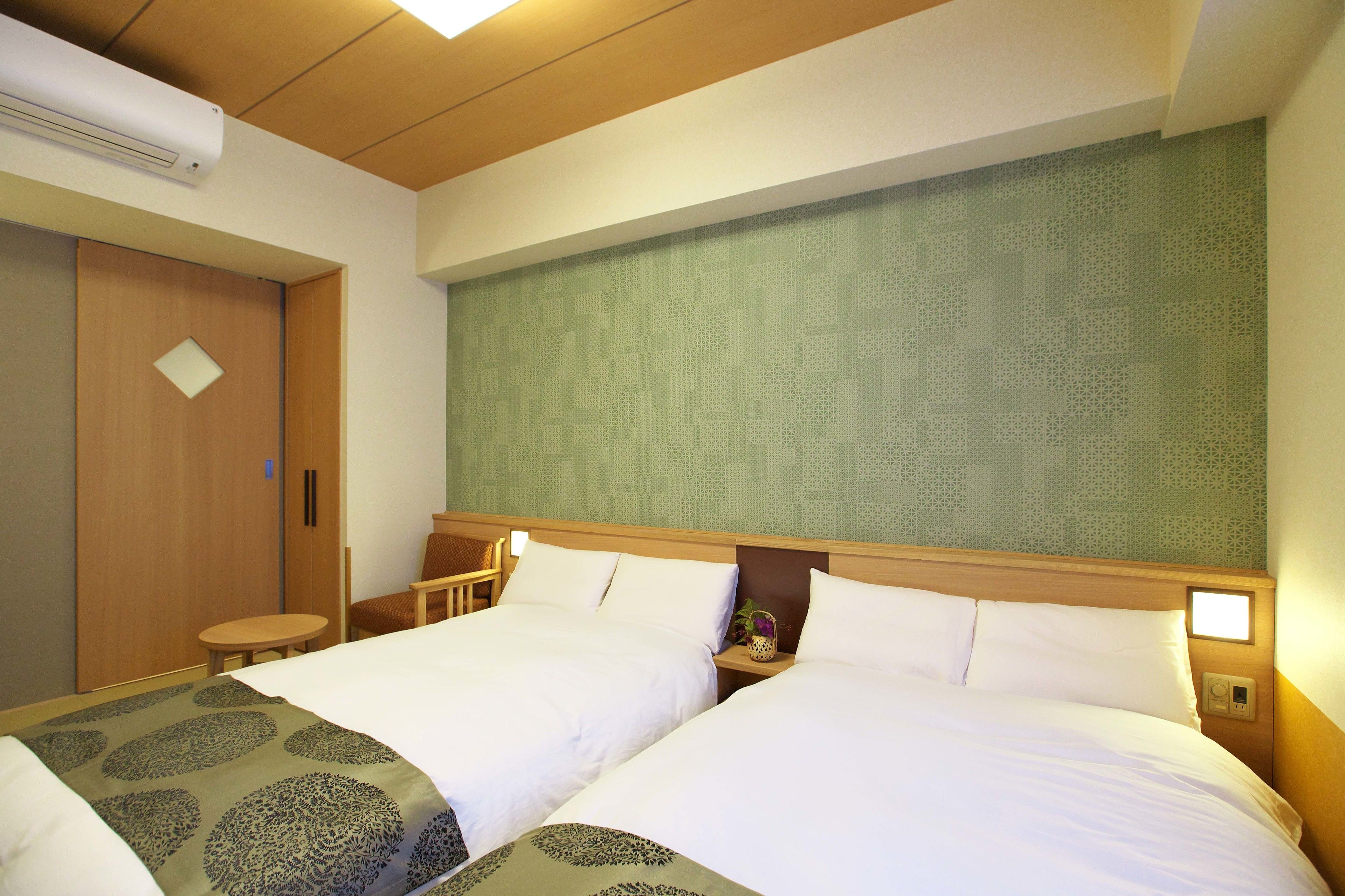 A hotel room with two beds, a wooden headboard, a small table, and a wall with a geometric pattern.