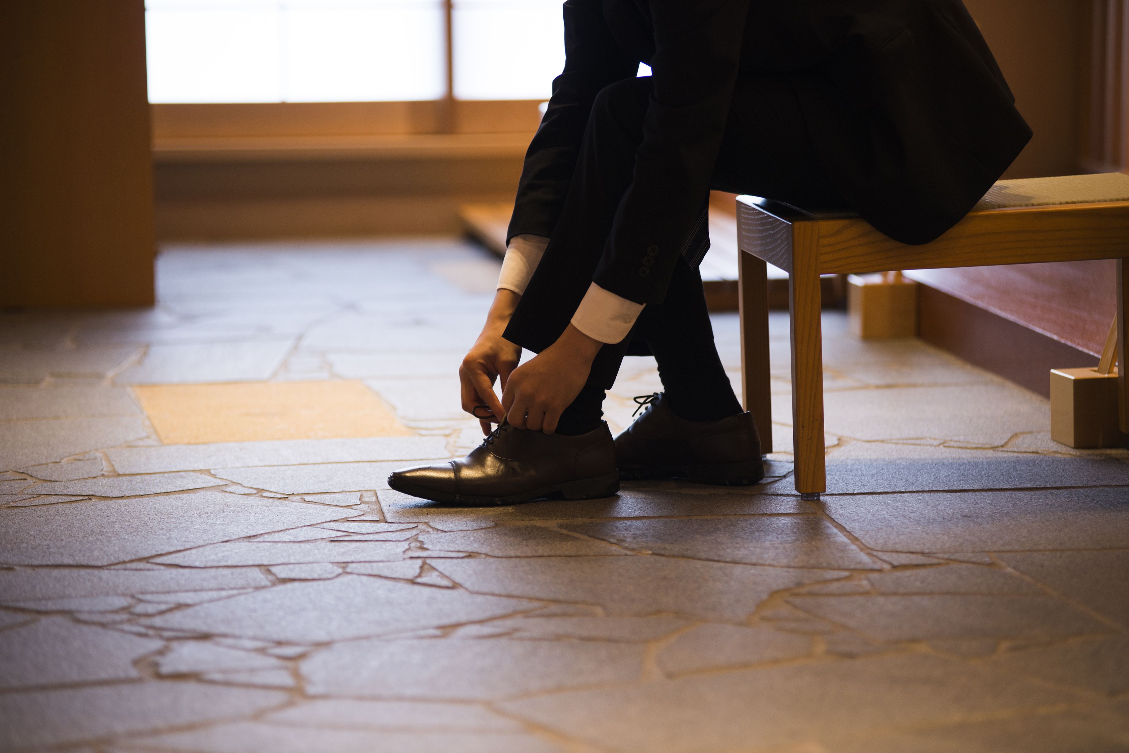 A person sitting on a wooden bench, tying their shoe.
