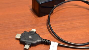 A black charging cable with a USB connector and a white power adapter on a wooden surface.