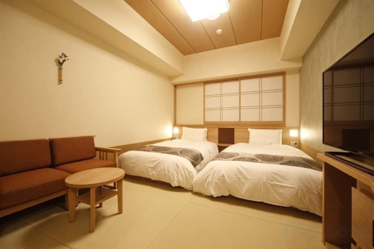 A hotel room with a sofa, two beds, a small table, and a TV.