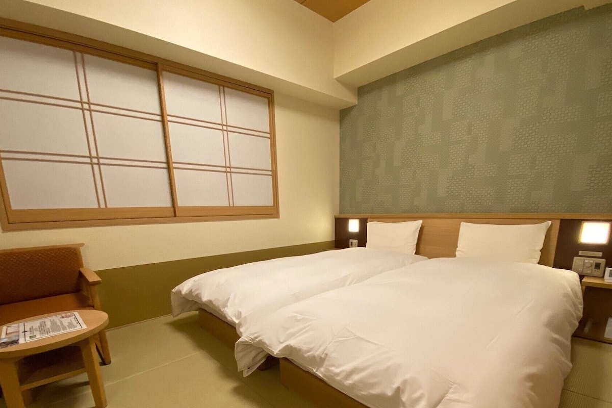 A hotel room with a large bed, a chair, a small table, and a window with a view.