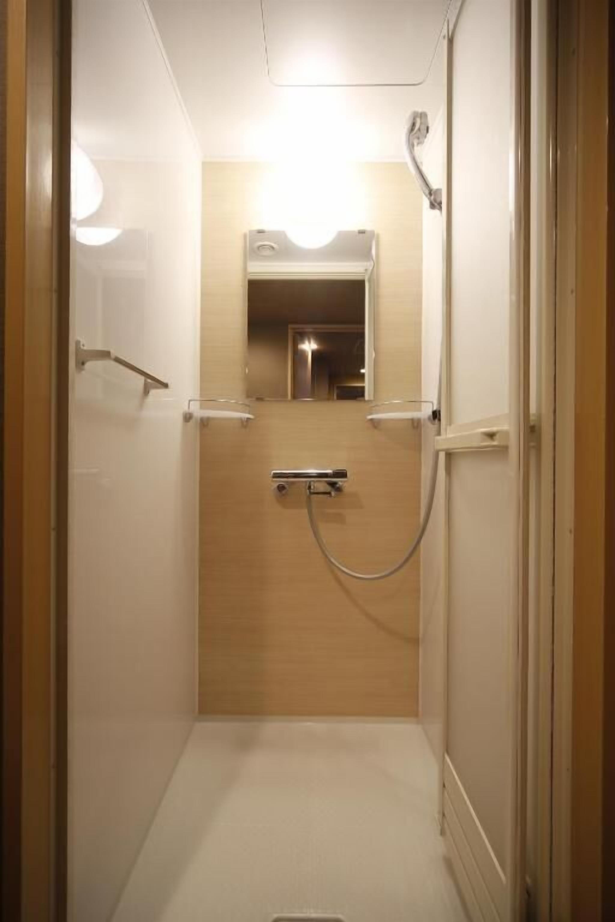 A narrow, enclosed bathroom with a shower, a mirror, and a toilet.
