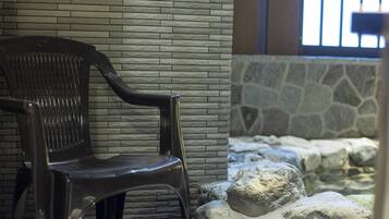 A black plastic chair against a textured stone wall, with a stone wall and rocks in the background.