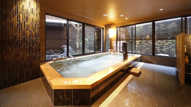A hot tub with a wooden bench, large windows, and a view of a garden. - Onyado Nono Nara Natural Hot Spring (Nara)