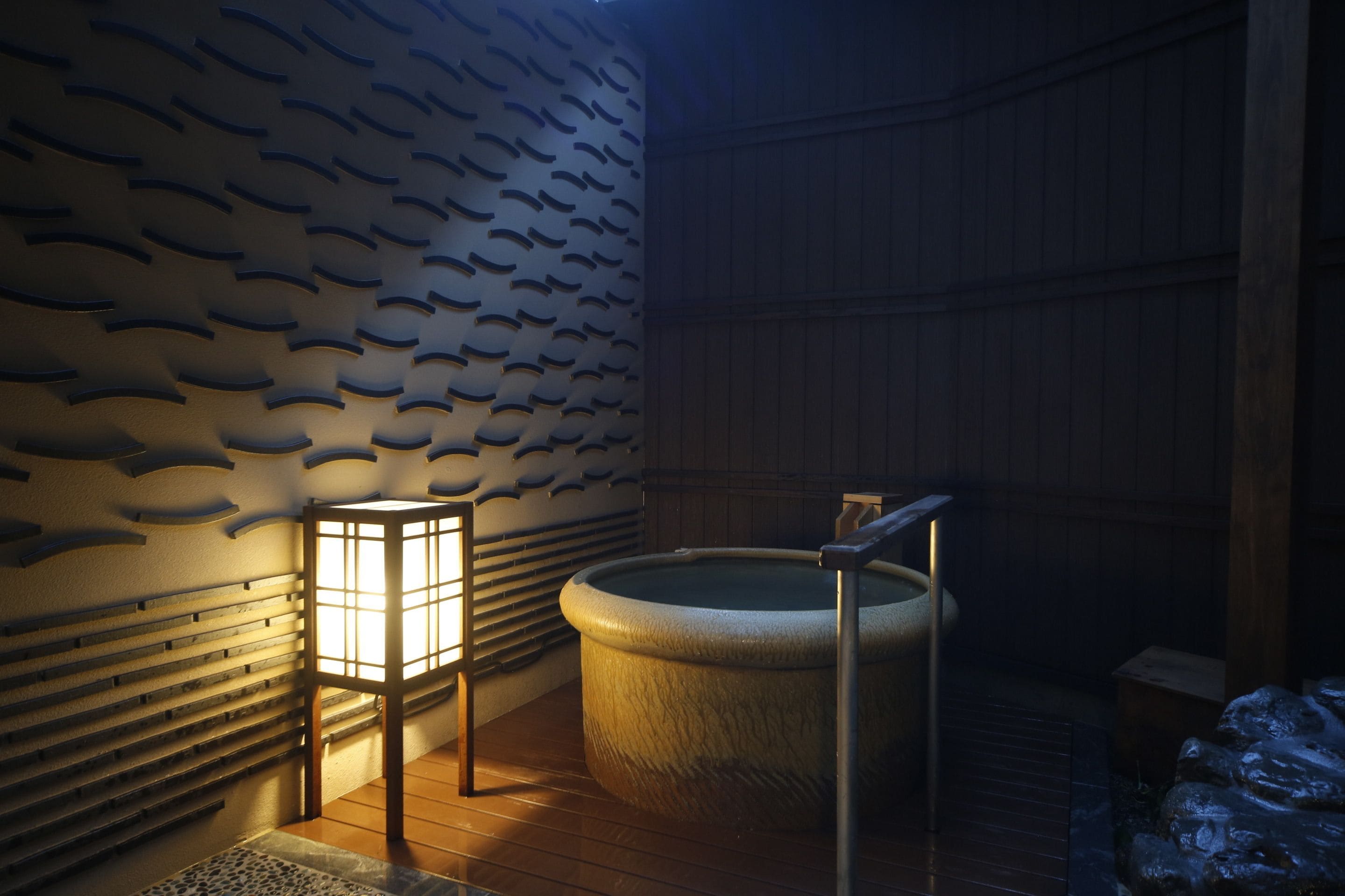 Un onsen japonés tradicional con interior de madera, una fuente termal de piedra y suelo de baldosas.