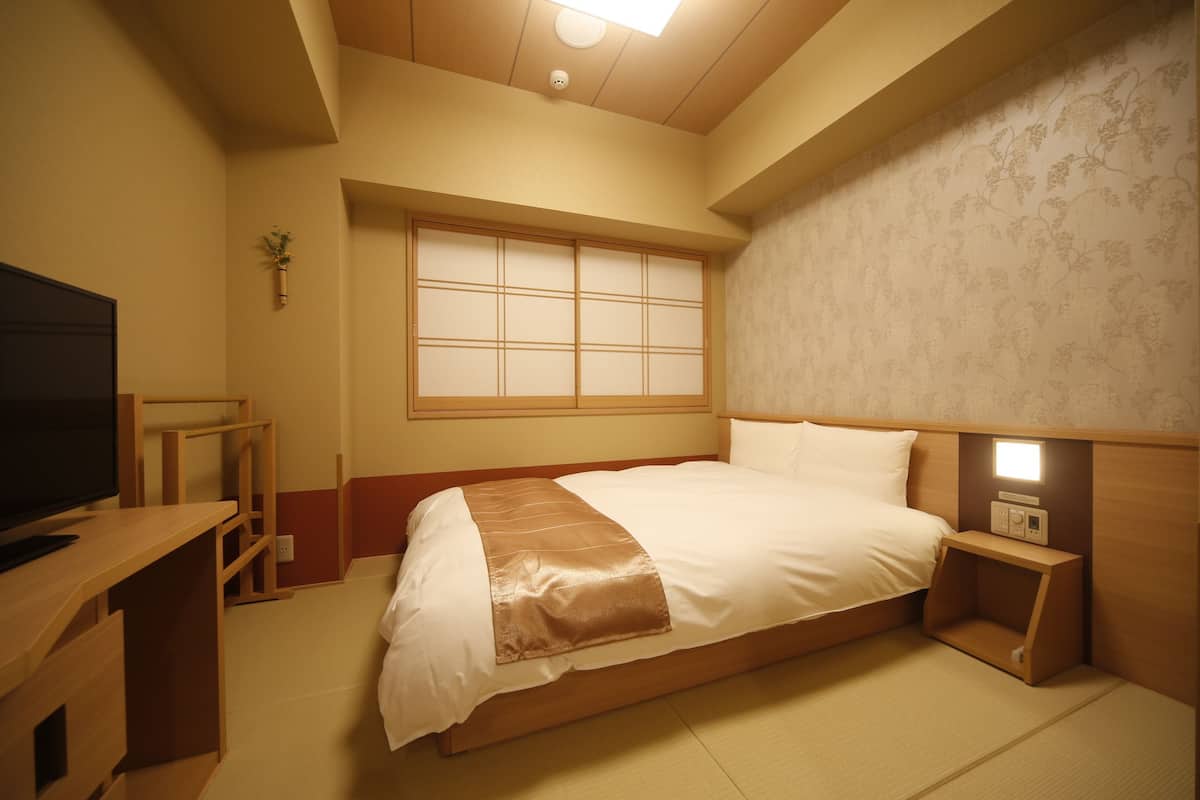 A hotel room with a bed, bedside table, TV, and a window with a view.
