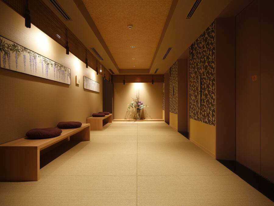 A hallway with a wooden bench, a vase with flowers, and a wall with a floral pattern.