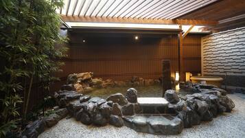 A traditional Japanese onsen with a stone bath surrounded by rocks, wooden walls, and bamboo plants.