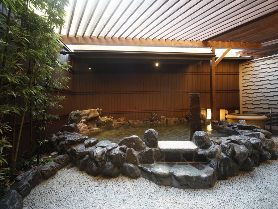 A traditional Japanese onsen with a stone bath surrounded by rocks, wooden walls, and bamboo plants.