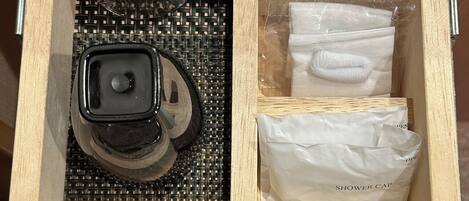 A wooden drawer with compartments containing a razor, a shower cap, a toothbrush, and a plastic bag.