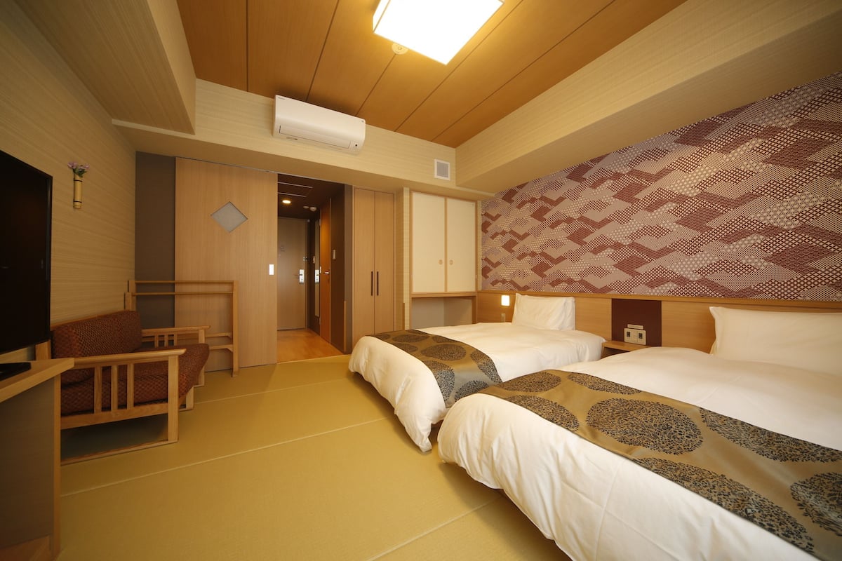 A hotel room with two beds, a TV, a desk, and a patterned headboard.