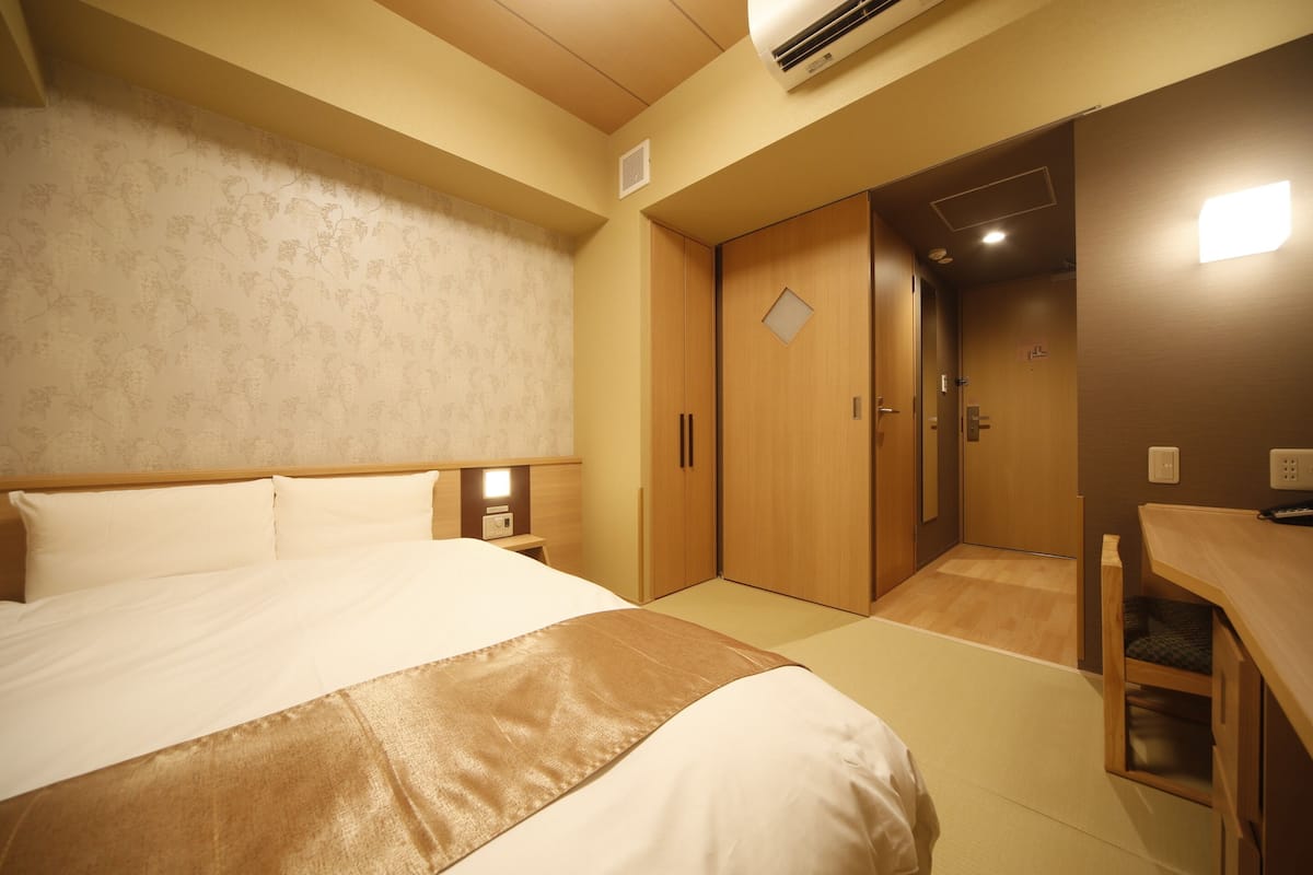 A hotel room with a large bed, wooden wardrobe, and a small desk with a chair.