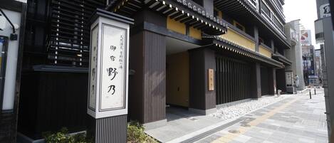Un edificio con elementos arquitectónicos tradicionales, un letrero con caracteres japoneses y un camino pavimentado.