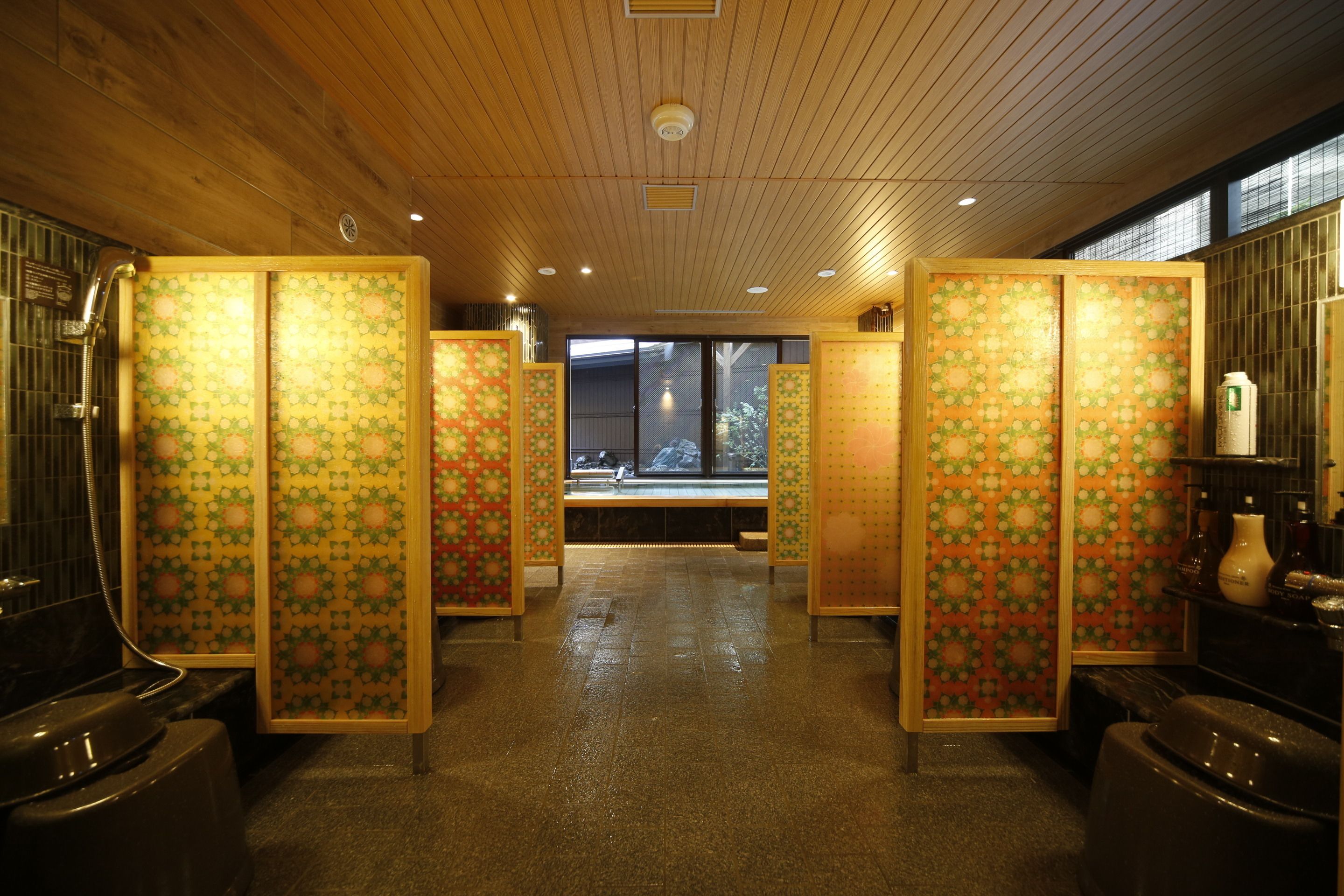 A traditional Japanese-style bathroom with sliding doors, a wooden ceiling, and a view of the outside through large windows.
