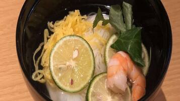 Un tazón de sopa con fideos, camarones, lima y hojas verdes.