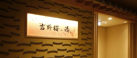 Una habitación con un diseño de pared de estilo japonés tradicional, un cartel enmarcado con caracteres japoneses y una puerta de madera que conduce a otra habitación.