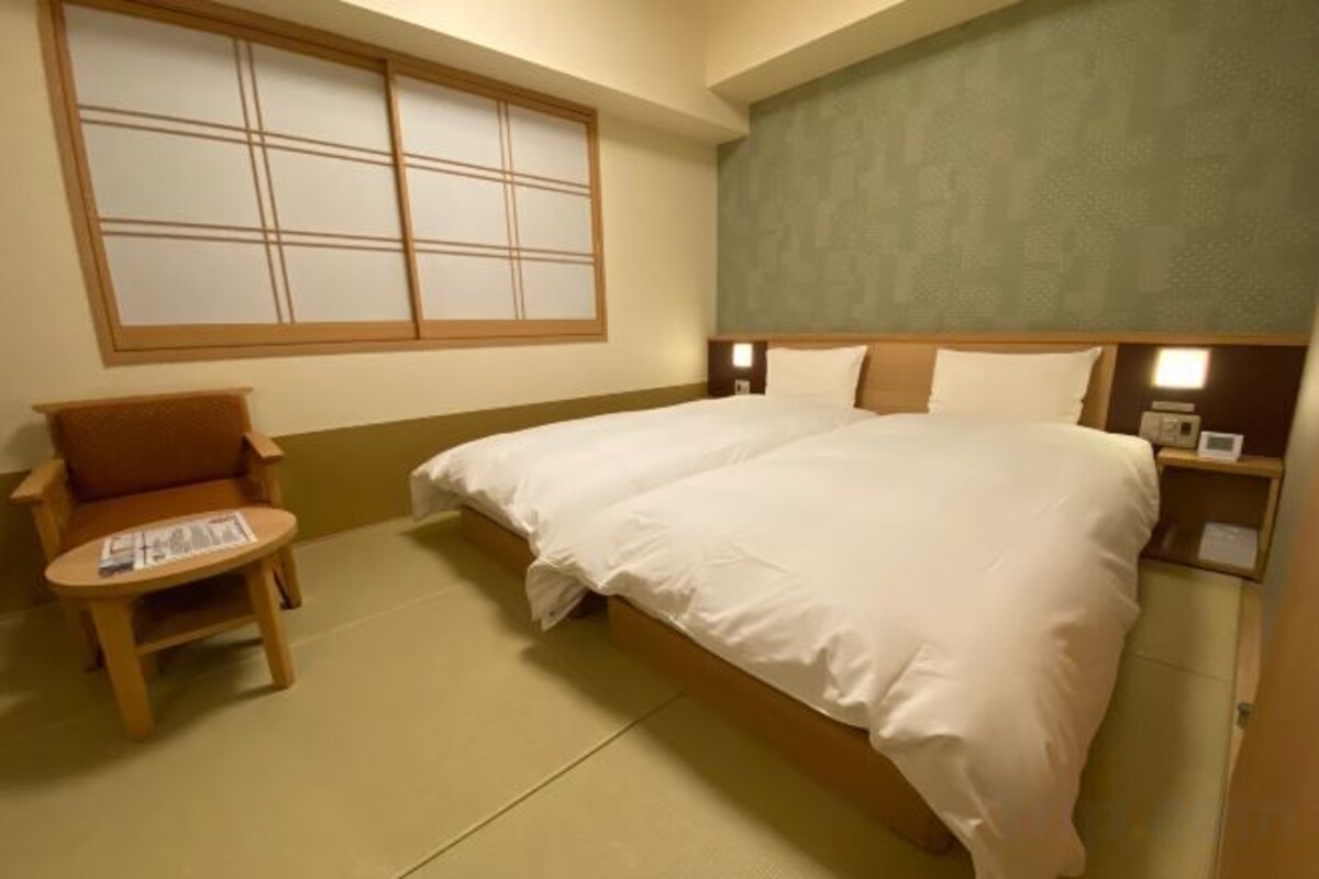 A hotel room with a bed, a chair, a small table, and a window.